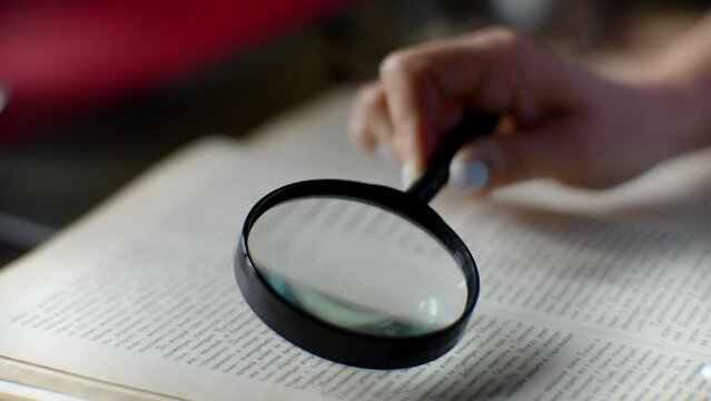 Woman reads book with magnifying glass in library	