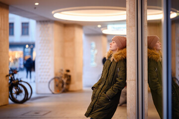 A young woman pauses for reflection in an urban passageway, her image mirrored in the glass