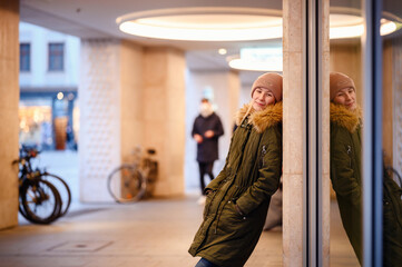 Fototapeta premium A young woman pauses for reflection in an urban passageway, her image mirrored in the glass