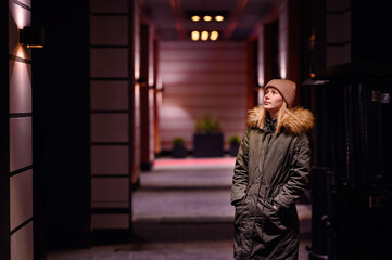 Woman takes a contemplative walk in an illuminated city alley at night, with warm lights above