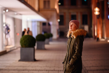 Obraz premium Young woman enjoys a serene walk past boutique windows on a beautifully lit city street at night