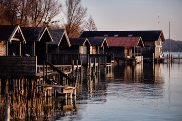 Evening light casts a glow on rustic boathouses lined along a tranquil lake