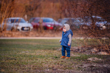 Naklejka na ściany i meble A curious toddler in a hooded jacket stands alone in a park during the early winter