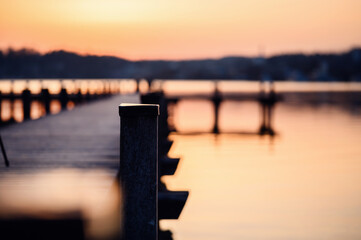 Golden sunset light bathes a wooden pier extending into a calm lake, with soft focus