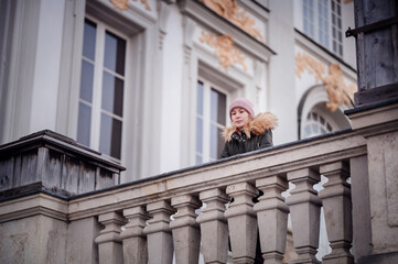 A pensive woman leans on a classic stone balcony, gazing out over the historic cityscape
