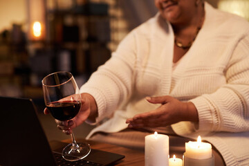 Close up of mature Black woman clinking wine glass to screen while talking by video chat and...