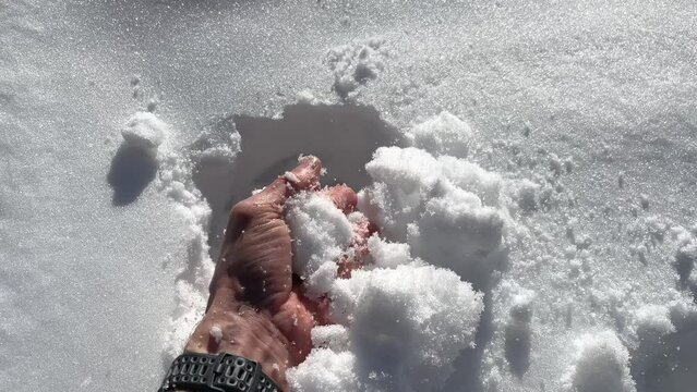 A bare hand takes fluffy white snow from the snowy ground in slow motion.