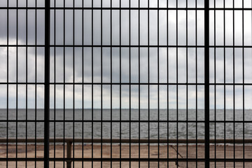 View of the sea through the bars of a prison window with a cloudy sky.