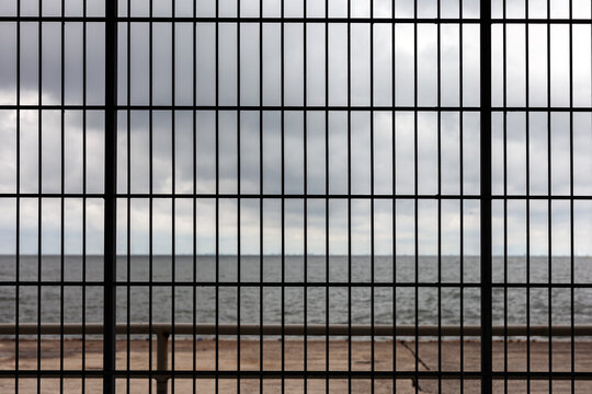 View of the sea through the bars of a prison window with a cloudy sky.