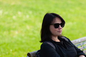 Portrait of a beautiful young woman in sunglasses sitting on a bench in the park