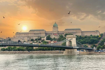 Photo sur Aluminium brossé Széchenyi lánchíd Szechenyi Chain bridge over the Danube River in the city of Budapest. Urban landscape with old buildings, St. Stephens Basilica and opera domes. Reddish sky and flying birds in the background. Hungary