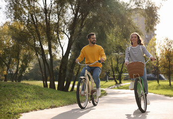 Beautiful couple riding bicycles in park, space for text