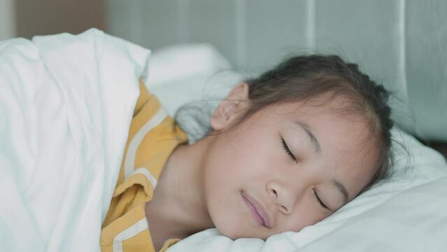 Close up face of adorable and pretty asian kid girl who is comfortably sleep in her bed in the beautiful morning shows concept of resting and relaxation of child with carefree and innocence.