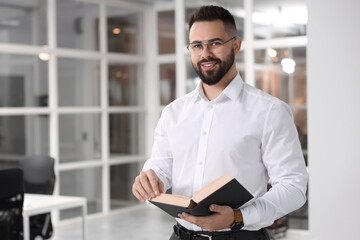 Fototapeta na wymiar Portrait of smiling man with book in office, space for text. Lawyer, businessman, accountant or manager