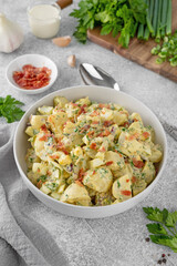 Salad of potatoes, eggs, bacon and fresh herbs with mayonnaise and yogurt dressing in a bowl on a gray concrete background.