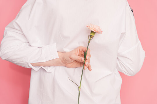 Lady holding one carnation behind her back against pink background.