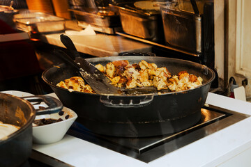 Open kitchen of restaurant or cafe in Vienna, Europe. Big black frying pan with traditional Viennese Kaiserschmarrn. Preparation of shredded sweet pancakes. View through the window from the street