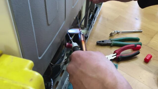 Fixing the refrigerator that not cooling enough by recharging Freon tube. Master attaches a tube with freon with a soldering iron