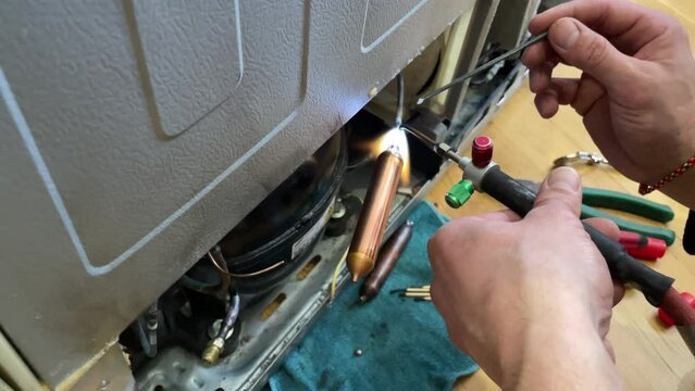 Fixing the refrigerator that not cooling enough by recharging Freon tube. Master attaches a tube with freon with a soldering iron