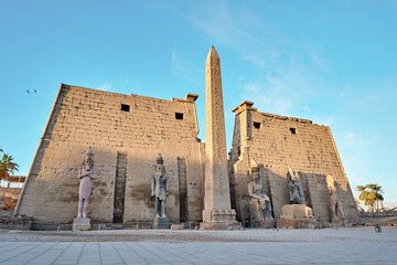 Luxor Temple Ramses statues. Statues at the Temple of Amun-Ra at Luxor. Egypt.Seated statue of Ramesses II by the First pylon of the Luxor Temple, Egypt - obrazy, fototapety, plakaty