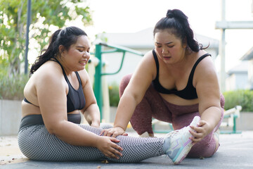 Close up shot of Asian oversized fat woman having an accident at her leg and her friend comes to help or support her. Oversized woman got an accident and her friend trying to do a first aid. - obrazy, fototapety, plakaty