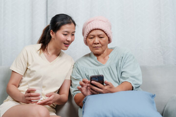 Asian daughter tenderly assists her mother, showing a tablet, highlighting a warm family caregiving...
