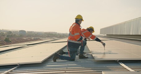 Two engineer workers in safety gear install solar panels on a rooftop, with a suburban landscape stretching out in the distance - obrazy, fototapety, plakaty