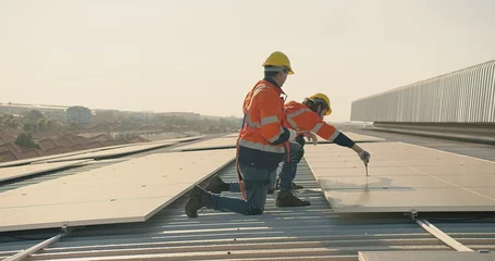 Fotobehang Two engineer workers in safety gear install solar panels on a rooftop, with a suburban landscape stretching out in the distance © HarryKiiM Stock