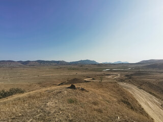 Photograph of Sandy Hills and Winding Dirt Road Under a Blue Sky, Sunny Day