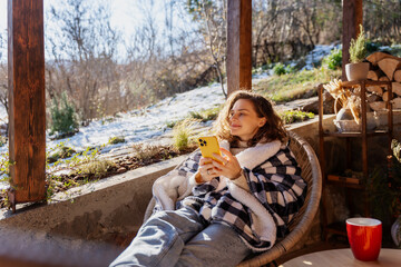 Young woman in a warm blanket on the terrace of a country house cottage enjoying the early spring...