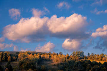Lovely blue sky with clouds in the evening over the mountain hills with forest in the warm sunset light. - 728697075