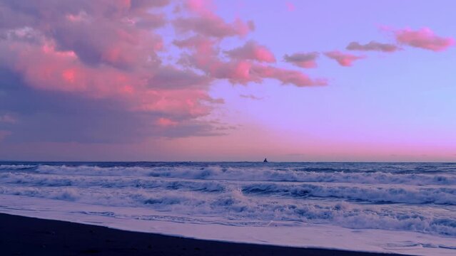 夕焼け空と砂浜に打ち寄せる波の先の水平線に烏帽子岩の見える湘南海岸の風景
