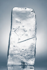 Crystal clear natural ice block in light blue tones on a white reflective surface. - 728698821
