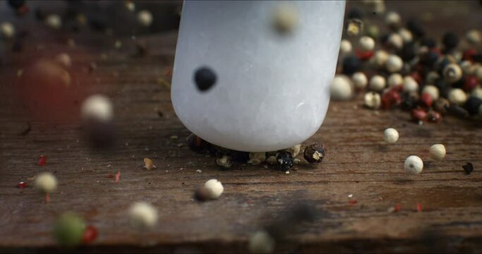 Super slow motion macro of dry mixed flavorful and aromatic peppercorn seeds bouncing with seed grinder on wooden table in rustic kitchen at 1000 fps.