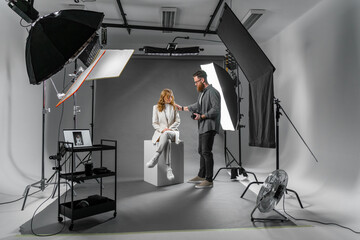 Professional photographer and beautiful model on fashion shoot in photo studio with lighting...
