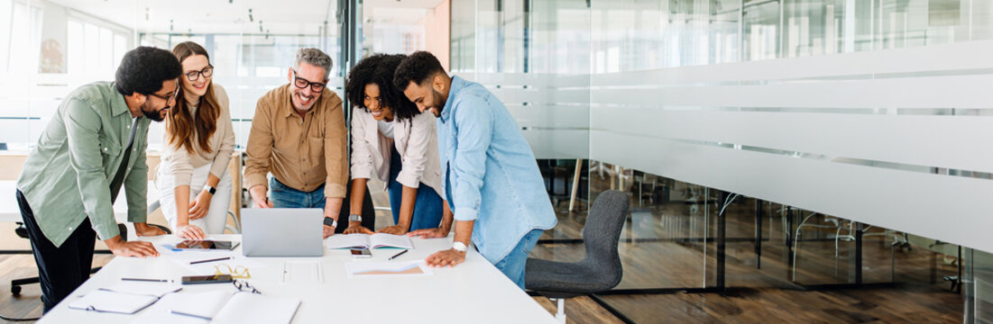 The diverse team of professionals engage in a dynamic exchange of ideas, with open laptops suggesting a collaborative working session. A productive and cooperative team during a creative brainstorm.