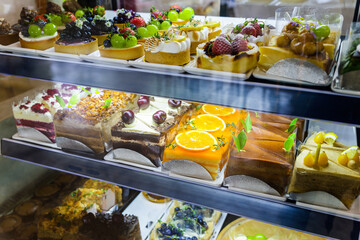 Various kinds of colorful fruit cakes and cheescake display in cake chiller in the restaurant