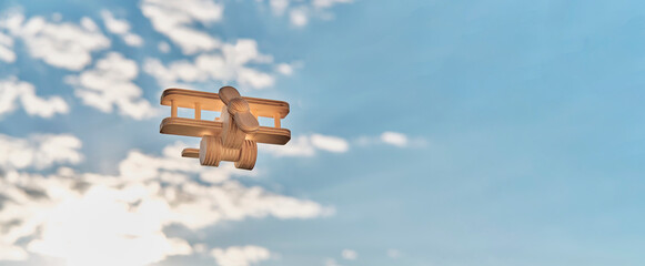 Wooden, made of plywood, small toy light aircraft biplane with propeller, flying in cloudy sky.