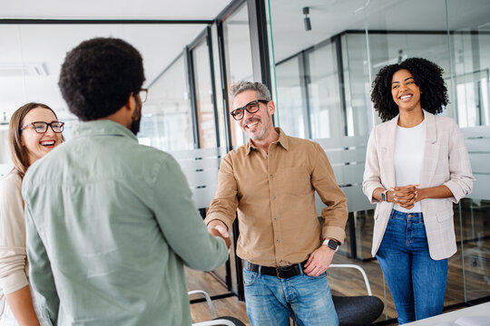 A friendly office environment is depicted where a team greets each other, shaking hands, showcasing the warmth and positive relationships between colleagues in a modern business setting.