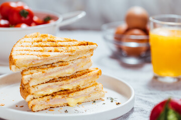 Toast sandwich with gouda cheese and turkey ham  on a bright background with ingredients in blurry background. Served with orange juice  and eggs