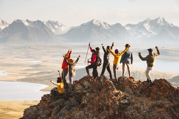 A large group of diverse tourists celebrates the completion of their climb to the top of the mountain with great view at sunset. Mixed ages and skills