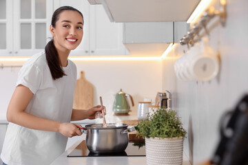 Fototapeta na wymiar Smiling woman cooking soup in light kitchen