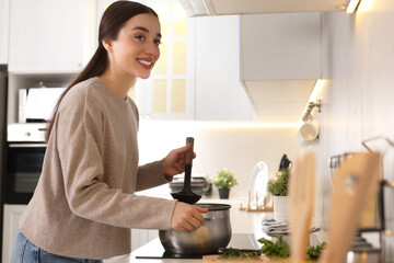 Smiling woman with ladle cooking soup in kitchen