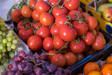 Tomates en rama, junto a racimos de uvas y otras frutas en un comercio de alimentación