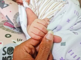 a father holding the hand of a newborn baby while he sleeps.