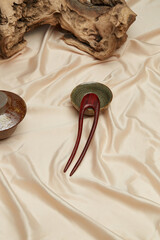 Close-up shot of a dark brown wooden hair pin in oriental style. A natural wood hair fork lies on a beige background near a bowls. Top view.