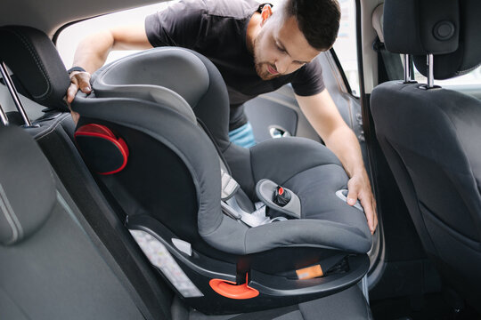 Man installs a child car seat in car at the back seat. Responsible father thought about the safety of his child. Man fasten seat belt on baby car seat