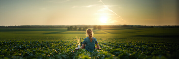 A female worker sits at a desk in the middle of lush, green farmland. A surreal image representing rural work from home and the technology shift that is affecting rural America and workplace culture - obrazy, fototapety, plakaty
