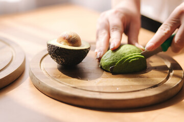 Close up of woman slicing avocado on wooden board at home. Vegetarian food concept. Avocado slice...