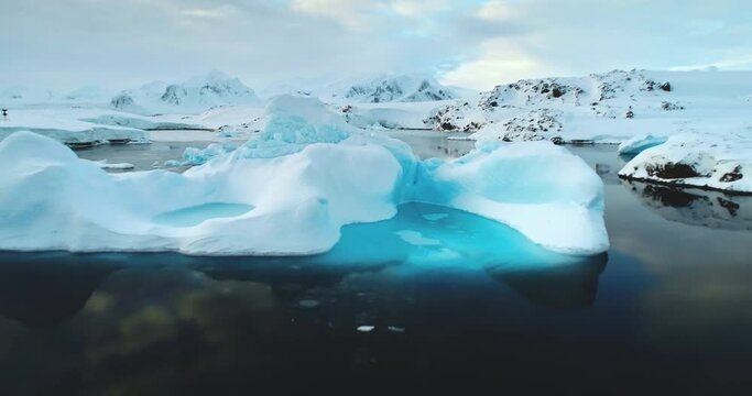 Glacier melting in Antarctica. Global warming. Climate change. Iceberg blue water cavity floating in cold water. Ice drift in polar ocean. Pristine Antarctic landscapes. Close up zoom out drone shot